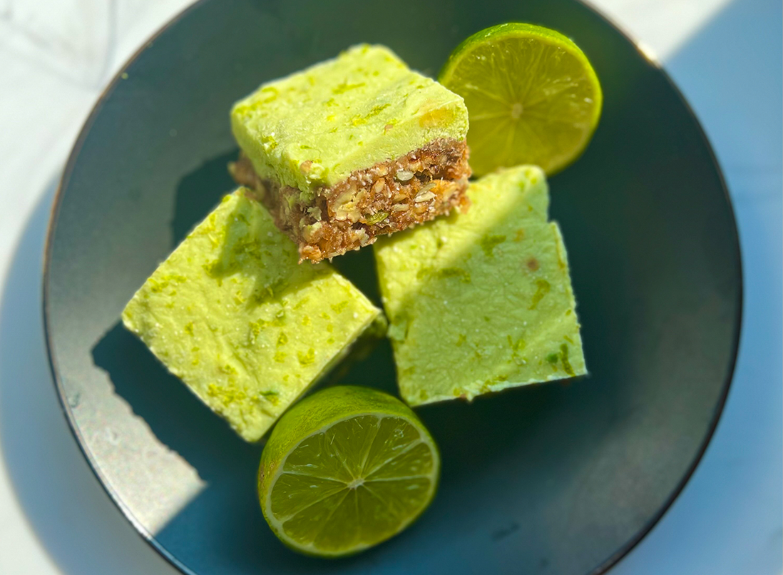 stack of 3 No-bake Key Lime Yogurt Bars on a dark green plate, with fresh limes in the sun