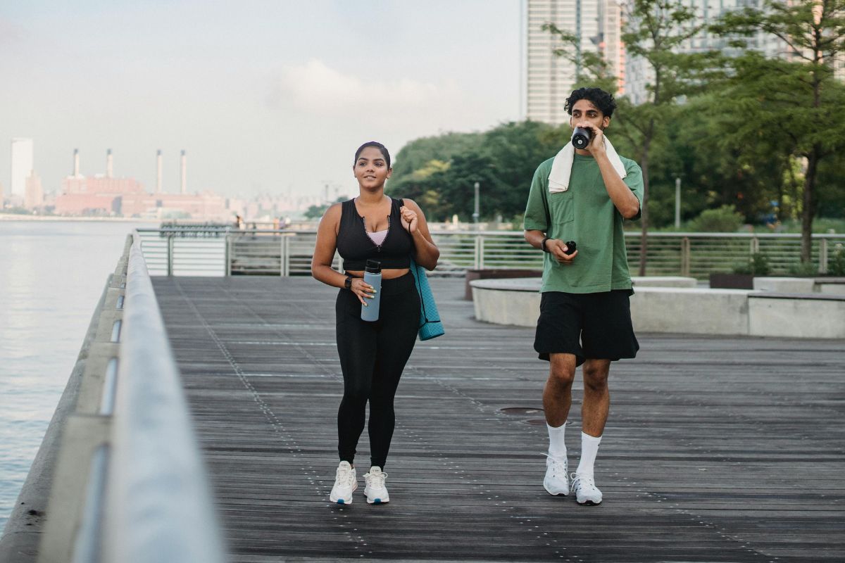 Woman and man in workout clothing walking along a board walk with water bottles in their hands